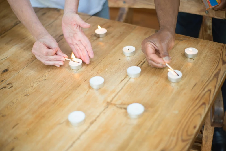 two people lighting candles on a wooden table, by Nina Hamnett, bringing people together, white, educational, as photograph