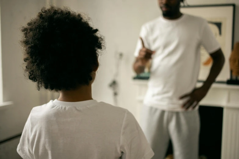 a man standing next to a little girl in a living room, pexels contest winner, black teenage boy, focus her back, dressed in a white t shirt, adversitement