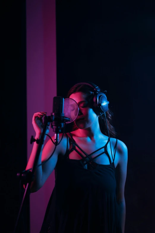 a woman in a black dress singing into a microphone, an album cover, pexels, studio ambient lighting, with headphones, university, colored lighting