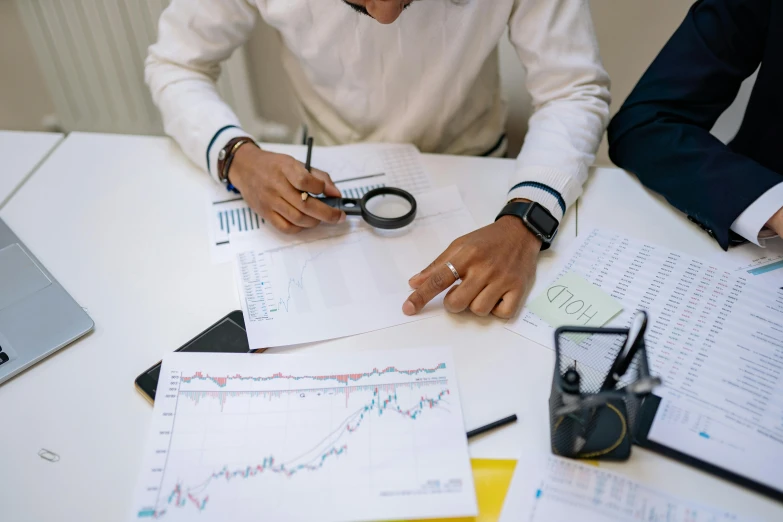 a couple of people sitting at a table with papers, trending on pexels, analytical art, wearing lab coat and glasses, graphs, thumbnail, trading