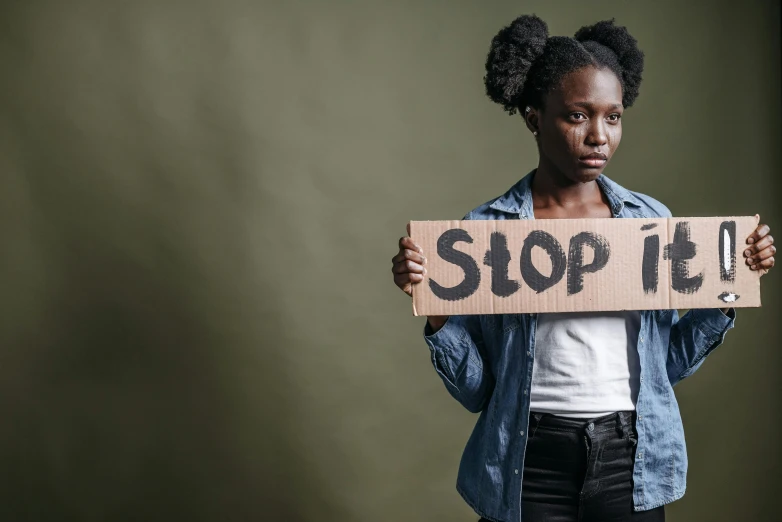 a woman holding a sign that says stop it, by Stokely Webster, shutterstock, dark skin, teenage no, poverty, instagram post