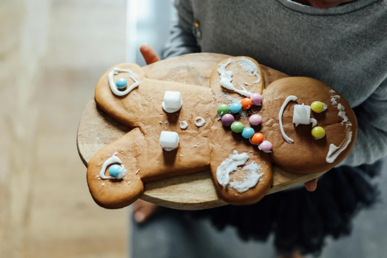 a close up of a person holding a plate of cookies, by Julia Pishtar, pexels contest winner, process art, gingerbread people, cheeky!!!, wooden, with sparkling gems on top