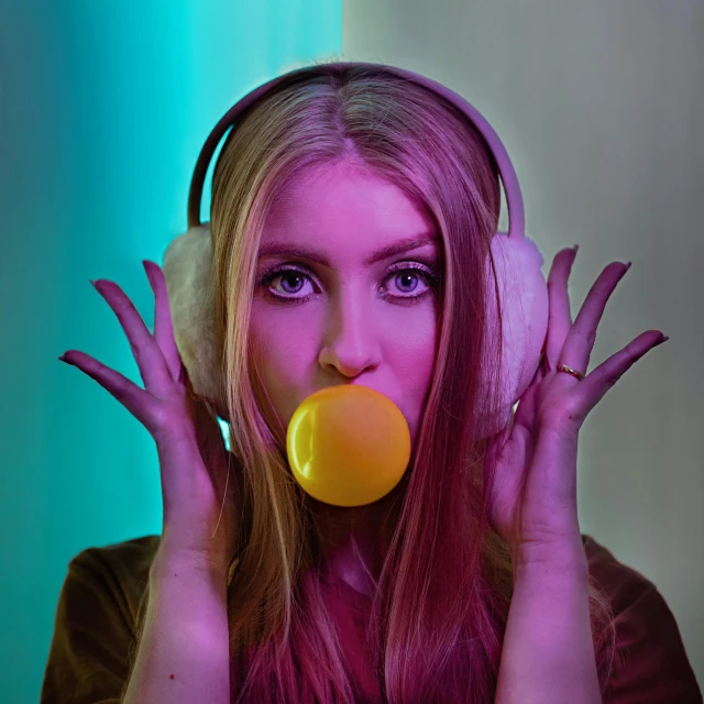 a woman with headphones blowing a bubble, an album cover, inspired by Elsa Bleda, pexels, pop art, banana, gaming headset, model posing, anna nikonova aka newmilky