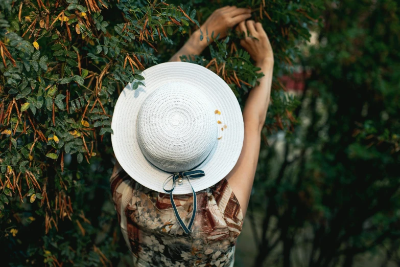 a close up of a person wearing a hat, a picture, by Emma Andijewska, pexels contest winner, hanging from a tree, with soft bushes, white sleeves, 3/4 view from below