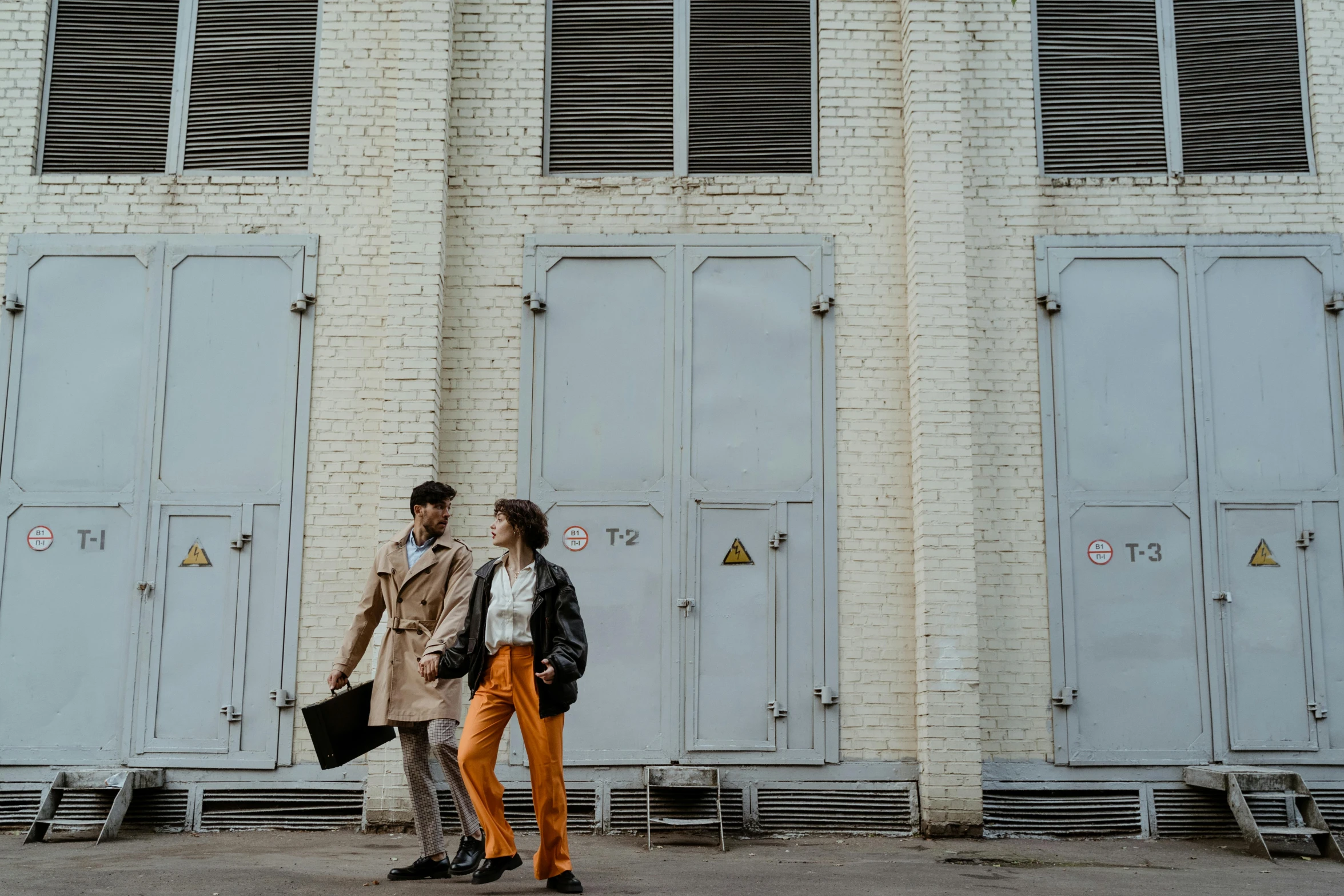 a couple of people standing in front of a building, by Lee Loughridge, pexels contest winner, brown pants, lockers, art deco factory, ad image