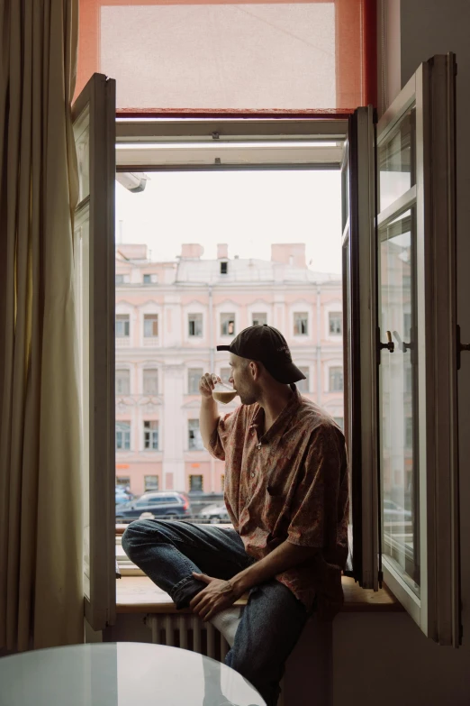 a man sitting on a window sill drinking from a cup, a picture, by Alexander Runciman, unsplash contest winner, caracter with brown hat, saint petersburg, flat mucha, hotel room