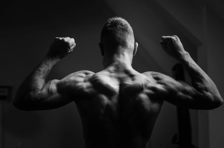 a man flexing his muscles in the dark, a black and white photo, by Adam Marczyński, pexels contest winner, wings on back, dramatic backgroung, back light, high quality upload
