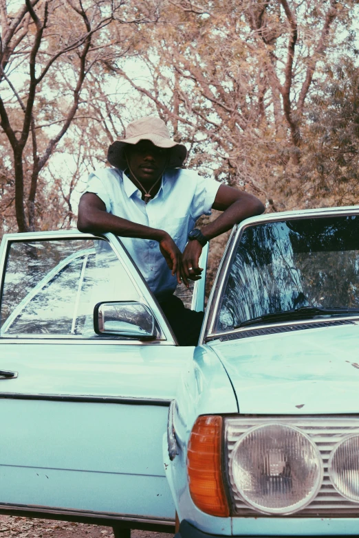 a man leaning on the hood of a blue car, an album cover, pexels contest winner, brown skin like soil, wears a destroyed hat, trending on vsco, very kenyan