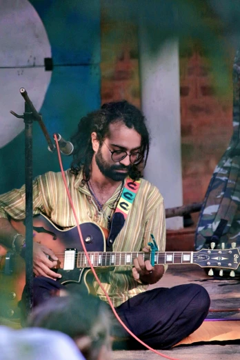 a man that is sitting down with a guitar, bengal school of art, a person at a music festival, profile image