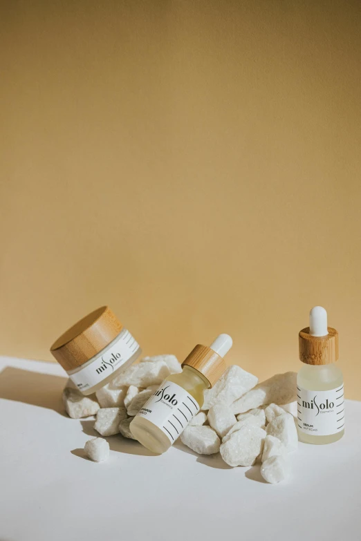 a couple of bottles sitting on top of a table, photoshoot for skincare brand, exploitable image, white rocks made of bone, label