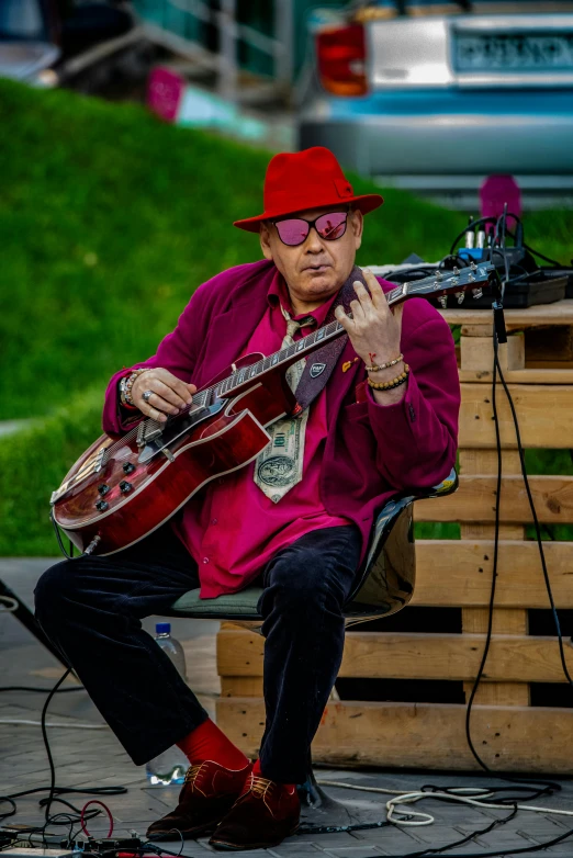 a man sitting on a bench playing a guitar, red sunglasses and a guitar, vic james, lights on, red suit