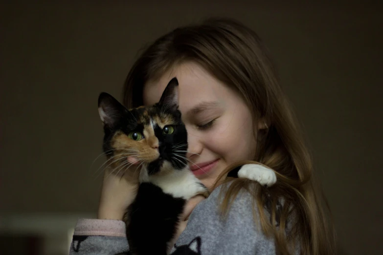 a girl holding a cat in her arms, by Julia Pishtar, pexels contest winner, calico cat, with kind face, black, mixed animal