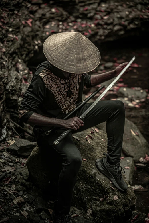 a man sitting on top of a rock holding a sword, an album cover, inspired by Kanō Hōgai, pexels contest winner, afrofuturism, pointy conical hat, cinematic outfit photo, vietnam, getting ready to fight