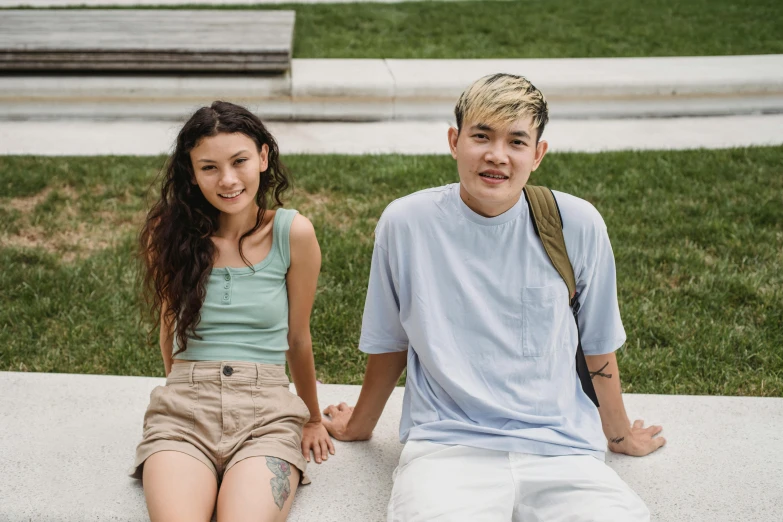 a man and a woman sitting on a bench, a colorized photo, trending on pexels, realism, tan skin a tee shirt and shorts, college students, half asian, looking confident