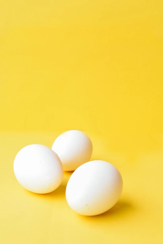 three white eggs on a yellow background, by Winona Nelson, trending on unsplash, epicurious, multiple stories, portrait shot, programming