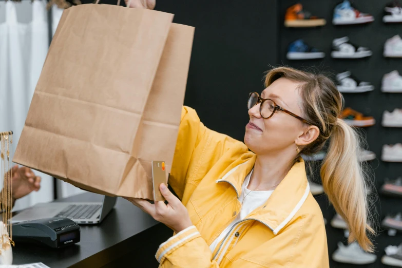 a woman in a yellow jacket holding a brown paper bag, at the counter, avatar image, candid photography, ecommerce photograph