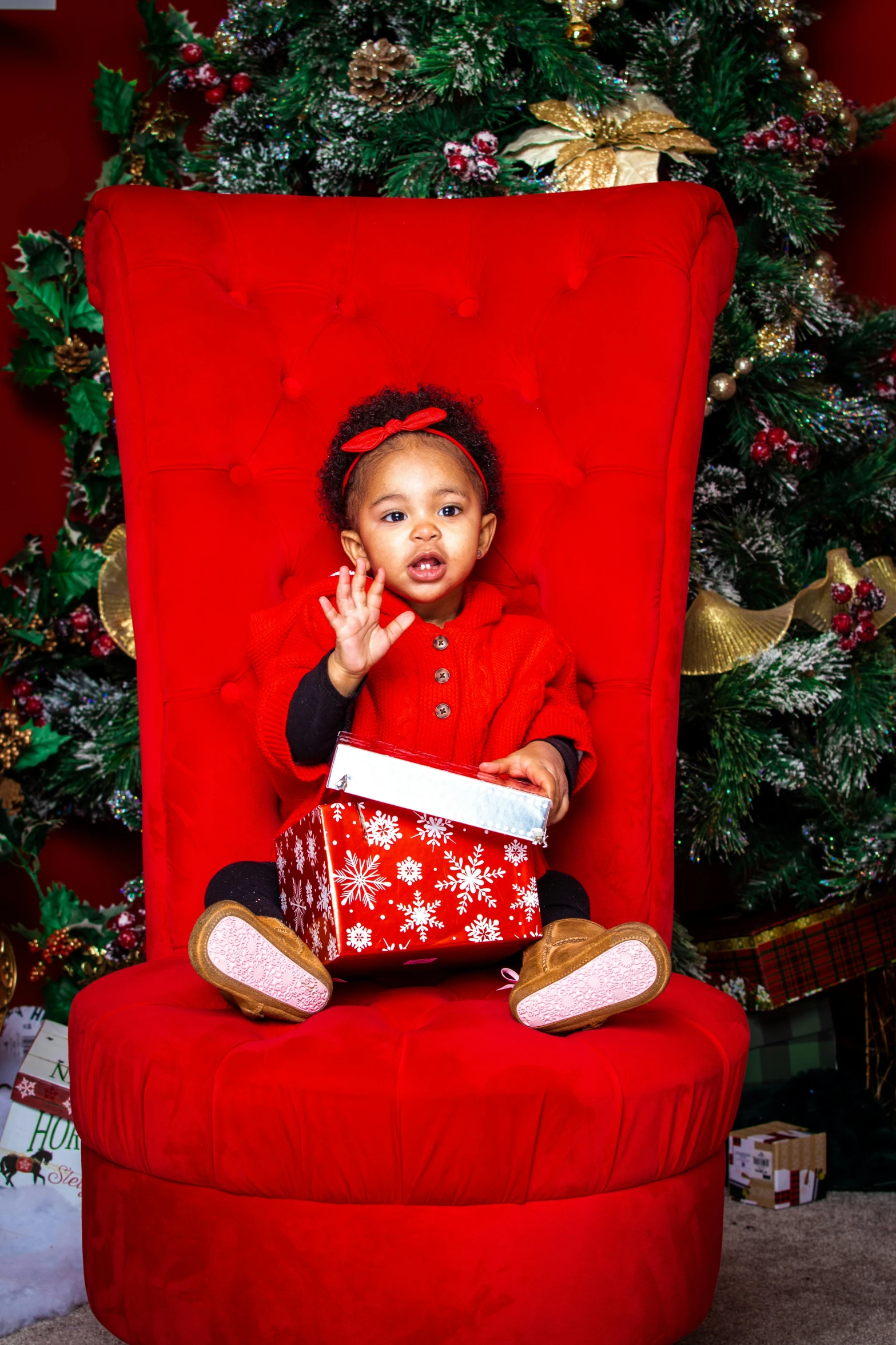 a little girl sitting on a red chair in front of a christmas tree, a portrait, shutterstock contest winner, portrait willow smith, 2 years old, giving gifts to people, on an icy throne