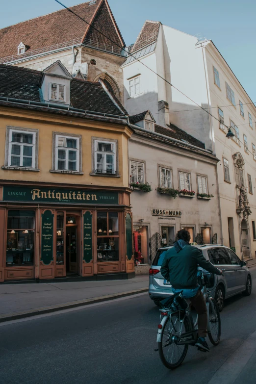 a man riding a bike down a street next to tall buildings, pexels contest winner, viennese actionism, old shops, medieval town, beer, bookshops