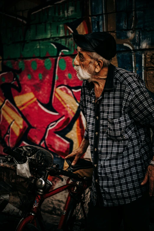 a man standing next to a bike in front of a graffiti covered wall, pexels contest winner, portrait photo of an old man, profile image, multi colour, an oldman