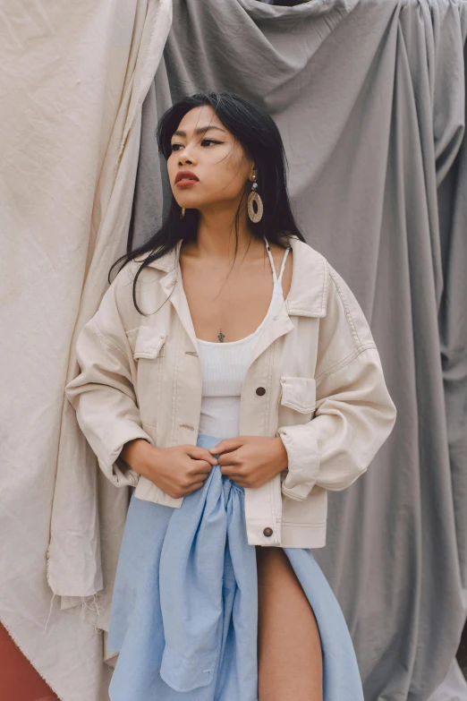 a woman standing in front of a curtain, an album cover, by Robbie Trevino, trending on pexels, jean jacket, south east asian with round face, wearing off - white style, fashion model pose