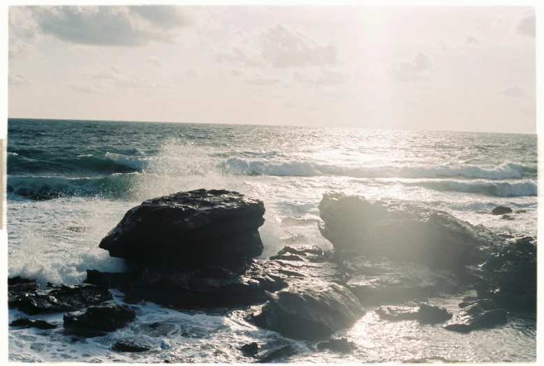 a large rock sitting on top of a beach next to the ocean, inspired by Elsa Bleda, unsplash, minimalism, tall backlit waves, australian beach, overexposed sunlight, medium format
