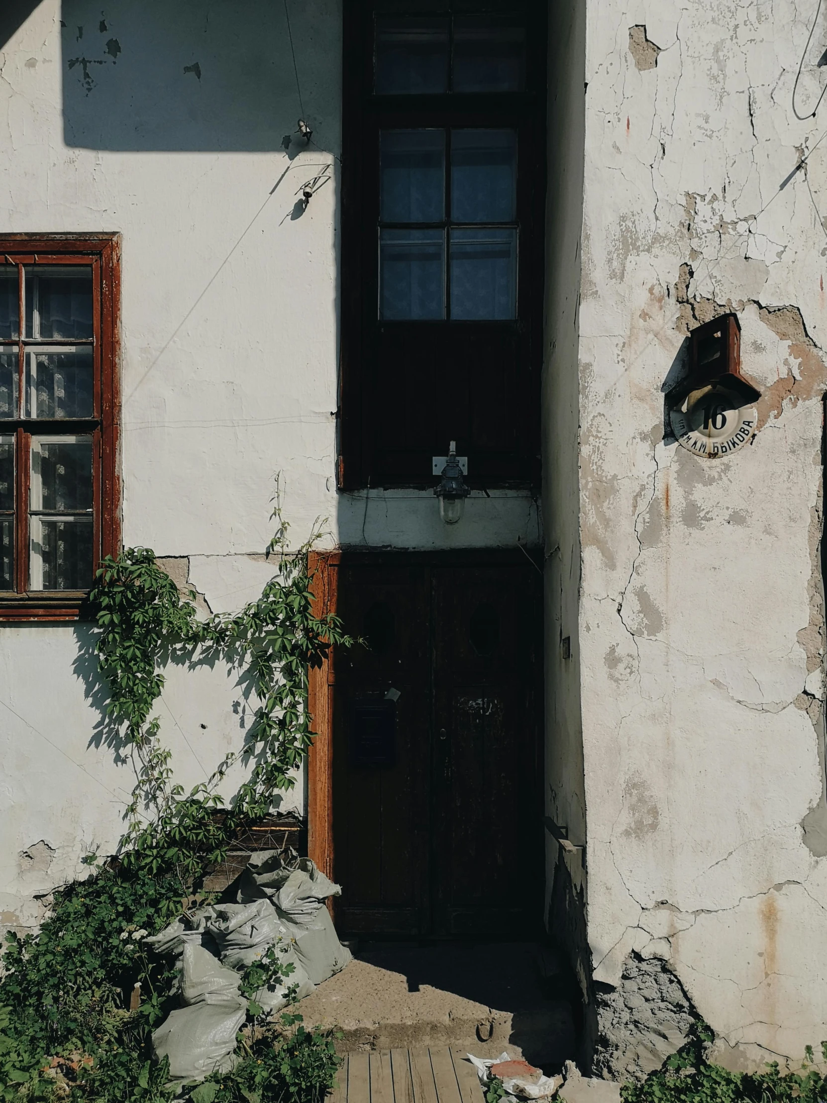 a white house with a black door and window, a photo, by Attila Meszlenyi, pexels contest winner, vine covered, damaged buildings, promo image, 90s photo