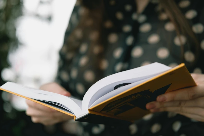 a woman holding a book in her hands, a picture, by Carey Morris, trending on unsplash, flat colour, detail shot, reading engineering book, fiona staples