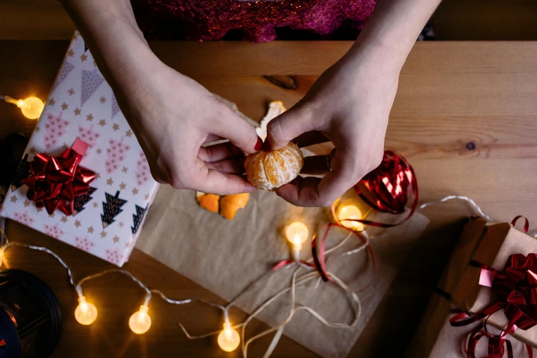 a person holding a doughnut on top of a table, christmas lights, holding a tangerine, crafting, press shot