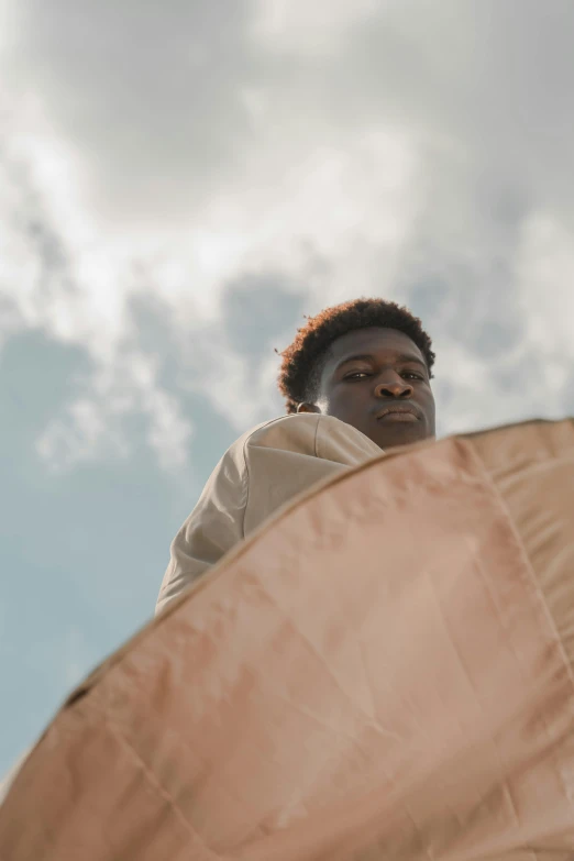 a man flying a kite on top of a sandy beach, an album cover, by Attila Meszlenyi, trending on unsplash, visual art, black teenage boy, standing with a parasol, brown skin, thoughtful