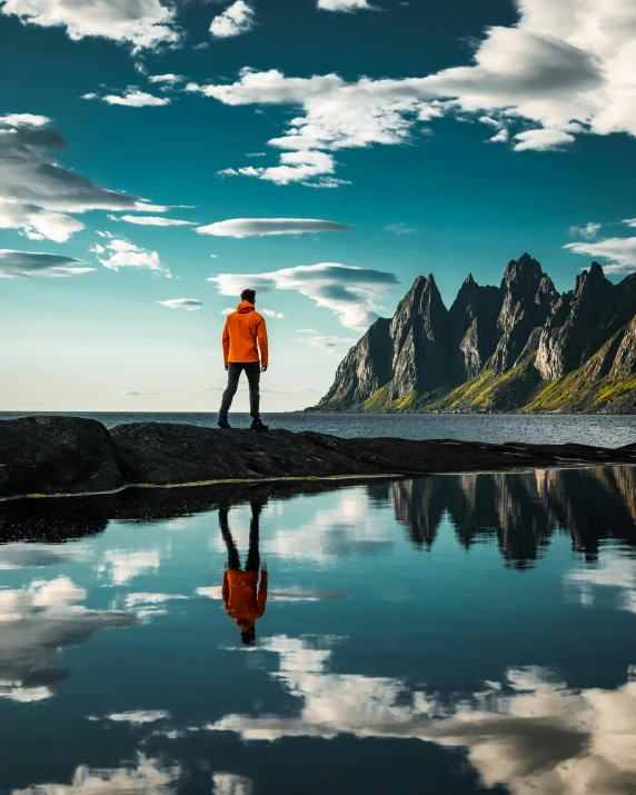 a man standing on top of a rock next to a body of water, by Harald Giersing, pexels contest winner, tall stone spires, highly reflective surface, today\'s featured photograph 4k, mountains and ocean