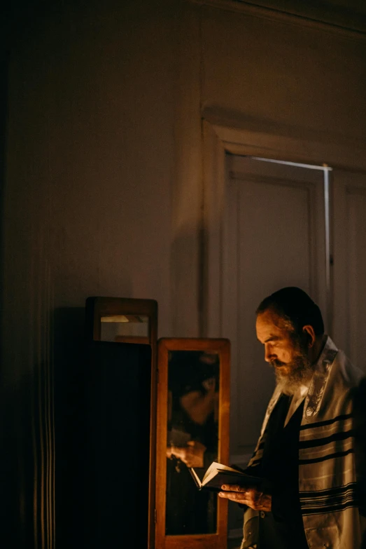 a man reading a book in a dark room, hebrew, with a mirror, lit up, holy ceremony
