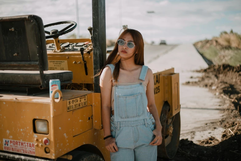 a woman standing next to a construction vehicle, pexels contest winner, wearing overalls, asian girl, avatar image, fashion photo