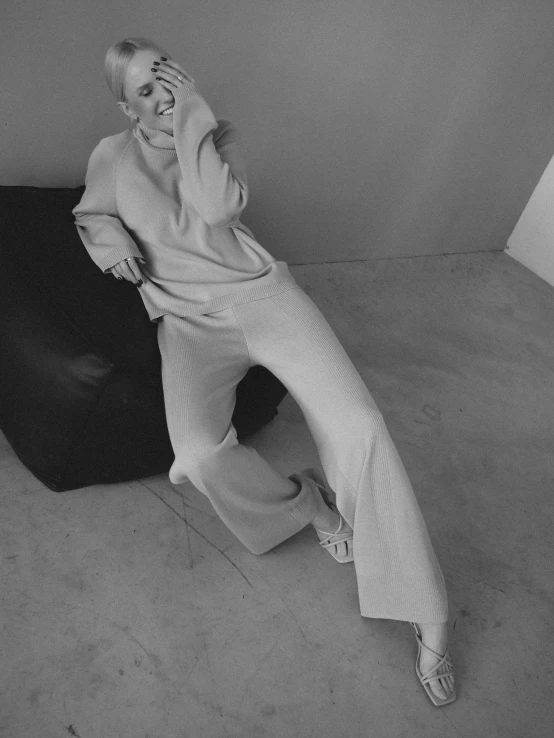 a woman sitting on a chair talking on a cell phone, an album cover, trending on unsplash, photorealism, high waist sweatpants, made in tones of white and grey, cropped wide sleeve, showstudio