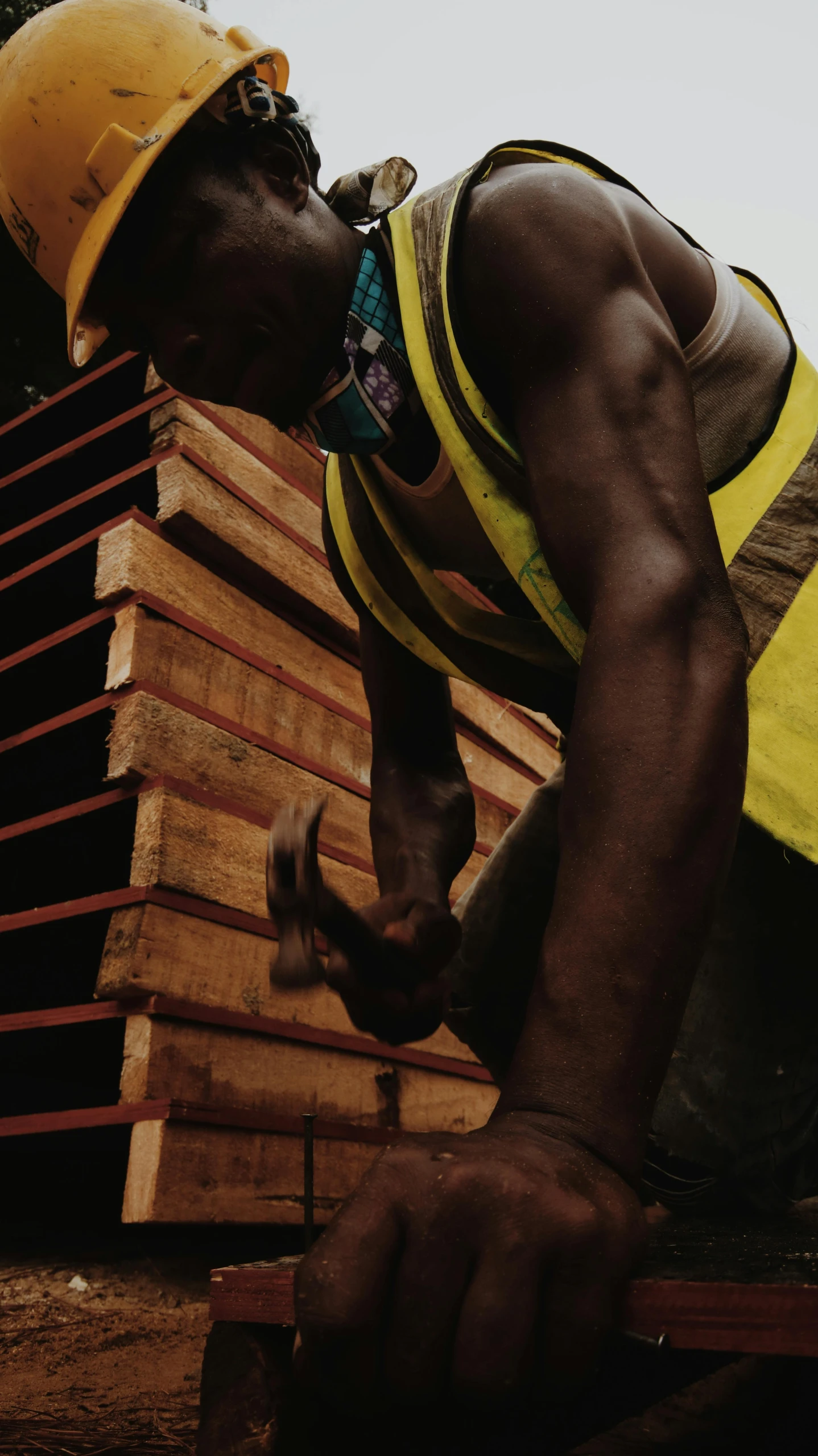 a man in a hard hat working on a piece of wood, an album cover, inspired by Afewerk Tekle, pexels contest winner, black vertical slatted timber, coloured photo, athletic crossfit build, african