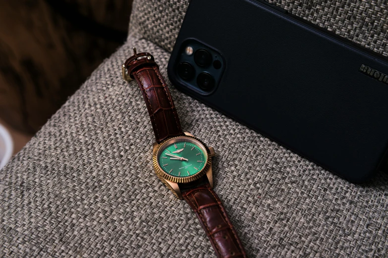 a watch sitting on top of a chair next to a cell phone, inspired by Henry Otto Wix, trending on pexels, renaissance, green and brown clothes, green magenta and gold, thumbnail, leather padding