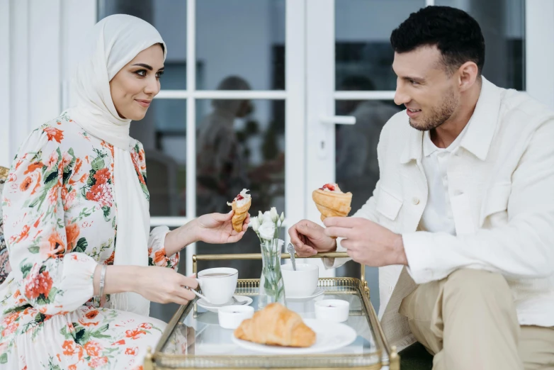 a man and a woman sitting at a table eating food, hurufiyya, white hijab, ice cream on the side, profile image, tea party