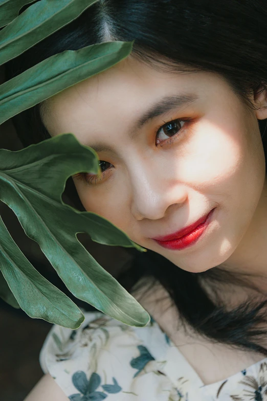 a woman holding a green leaf in front of her face, inspired by Ai Xuan, pexels contest winner, photorealism, light-red lips, ulzzang, high angle closeup portrait, lovingly looking at camera