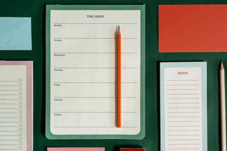 a green table topped with notepads and a pencil, by Doug Ohlson, trending on unsplash, orange details, in the style wes anderson, female calendar, green and red