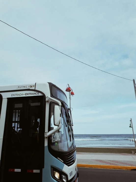 a bus driving down a road next to the ocean, 🚿🗝📝, standing near the beach, tram, full frame image