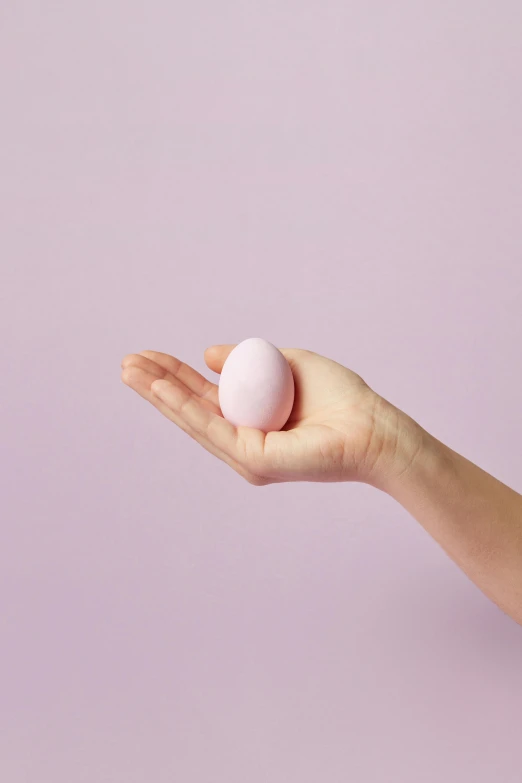 a person holding an egg in their hand, light pink, silicone skin, product shot, pink mist