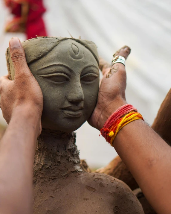 a close up of a person holding a clay sculpture, a statue, by Sunil Das, trending on unsplash, centered headdress, lgbtq, digging, holy ceremony