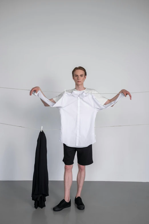 a man standing in front of a white wall, inspired by Jakob Emanuel Handmann, neo-dada, tied - up shirt, genderless, laundry hanging, production photo