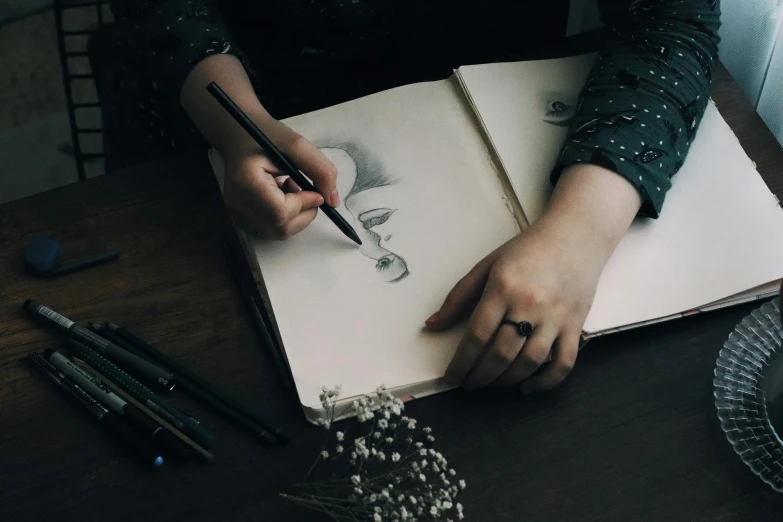 a woman sitting at a table drawing on a piece of paper, a drawing, by Adam Marczyński, pexels contest winner, drawing pictures on a notebook, rpg book portrait, drawing faces
