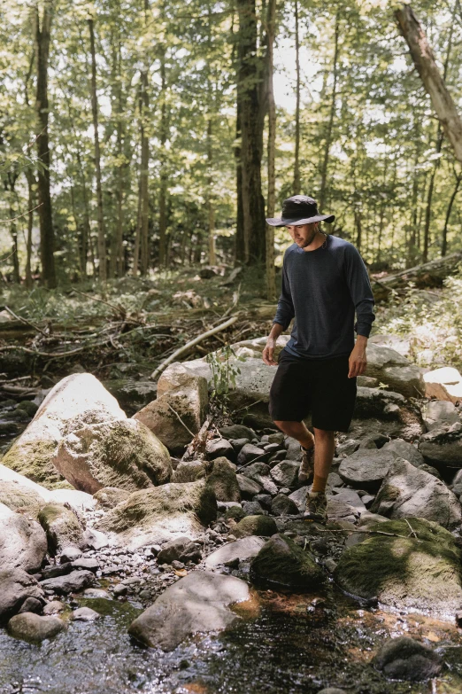 a man standing next to a stream in a forest, inspired by Asher Brown Durand, unsplash, baggy clothing and hat, ignant, boulders, walking