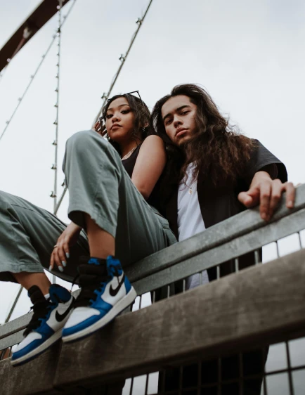 two women sitting next to each other on a bridge, an album cover, trending on pexels, sneaker photo, androgynous male, couple portrait, profile image