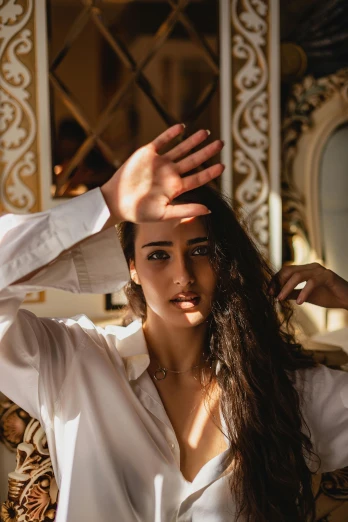 a woman putting her hair in front of a mirror, an album cover, by Julia Pishtar, trending on pexels, arabesque, wearing a white button up shirt, indian super model, soft backlight, hands on face
