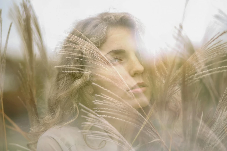 a woman standing in a field of tall grass, inspired by Elsa Bleda, unsplash contest winner, photorealism, her face framed with curls, portrait of ana de armas, 35mm double-exposure photo, medium format. soft light