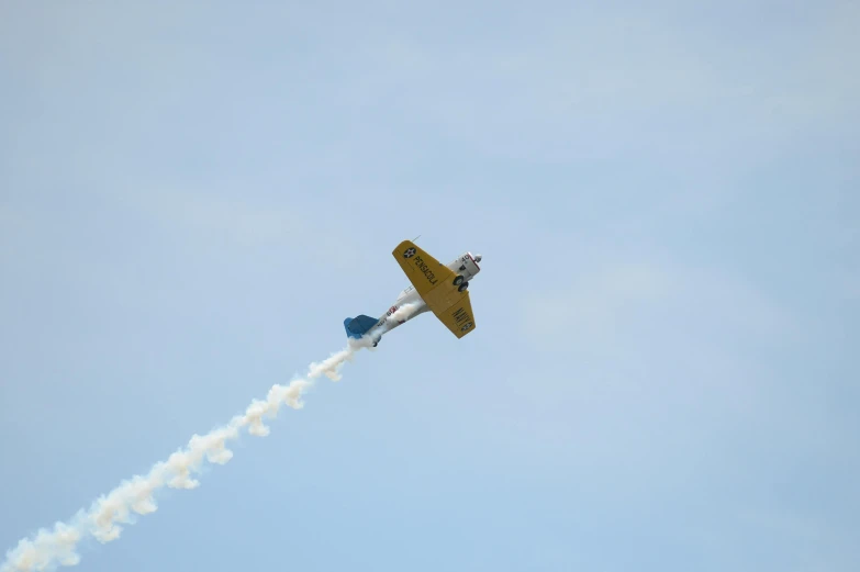 a small plane flying through a blue sky, a picture, by Neil Blevins, unsplash, figuration libre, smoke :6, yellow, acrobatic, 2022 photograph