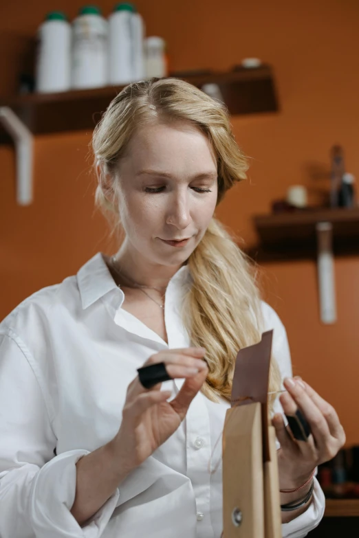 a woman in a white shirt working on a piece of wood, a photorealistic painting, inspired by Francesco Hayez, trending on pexels, apothecary, with professional makeup, holding a leather purse, kirsi salonen