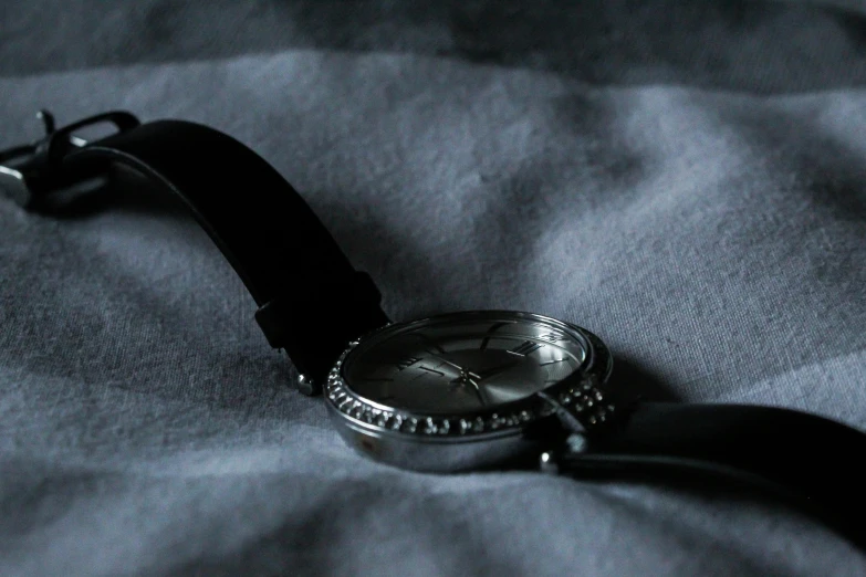 a close up of a watch on a bed, by Adam Marczyński, visual art, black and silver, thumbnail, lightweight, dainty